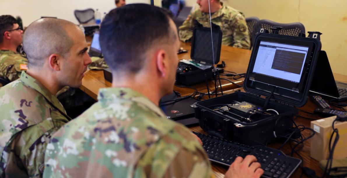 Soldiers work on the system that manages the Remote Access Drop Device placed on an unmanned aerial system and Spot, the robotic dog, during an Operational Readiness Assessment for the 11th Cyber Battalion