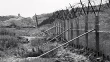 The barrier fence along the southern boundary of the Demilitarized Zone, Korea, in 1968. A guard tower stands in the distance. (Credit: U.S. Army)